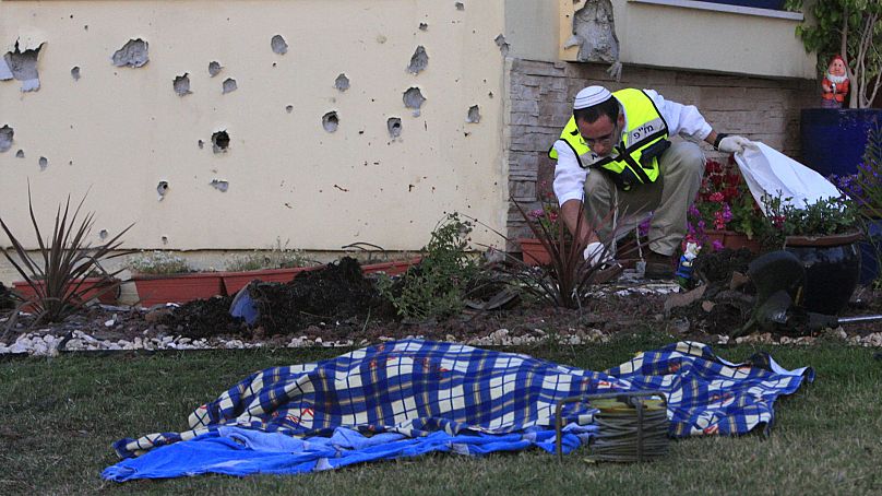 Un secouriste israélien examine les lieux alors que le corps d'un homme tué par un mortier tiré par des militants palestiniens à Gaza repose sur le sol devant sa maison à Kfar Aza.