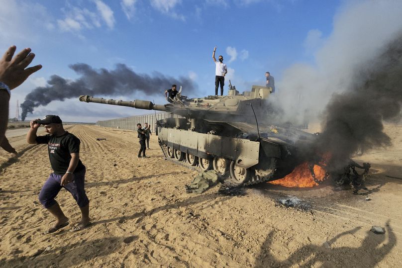 Des Palestiniens célèbrent devant un char israélien détruit à la barrière frontalière entre Israël et la bande de Gaza, le 7 octobre 2023.