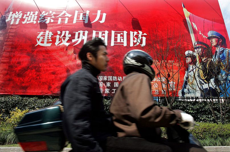 Des hommes roulent à moto devant un slogan du gouvernement en chinois 