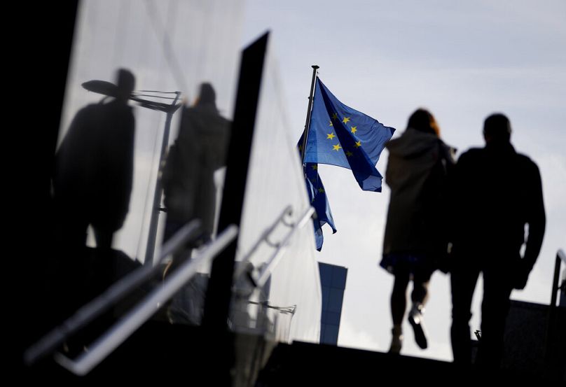 Un couple passe devant les drapeaux de l’UE devant le siège de l’UE à Bruxelles, octobre 2021