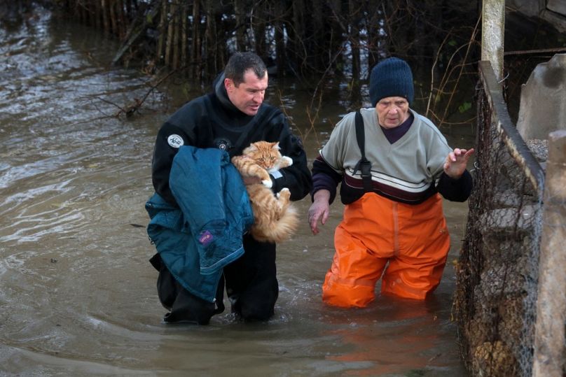 Un sauveteur transporte un chat et aide une femme lors de l'évacuation des habitants du village inondé de Pribrejnoe en Crimée le 27 novembre 2023, à la suite d'une tempête.