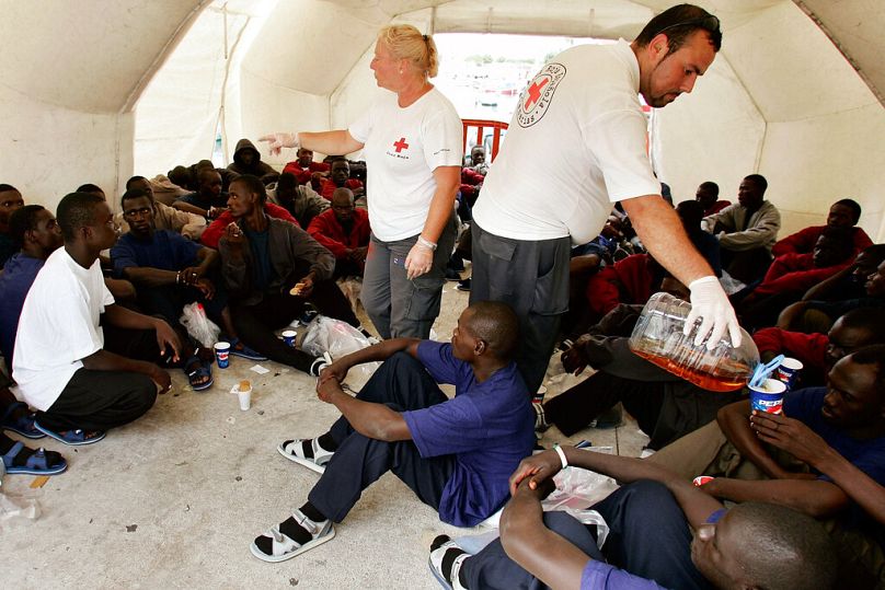 Des travailleurs de la Croix-Rouge se tiennent au milieu de certains des 105 candidats à l'immigration dans une tente après leur arrivée dans le port de Los Cristianos, sur l'île canarienne de Tenerife, en Espagne.