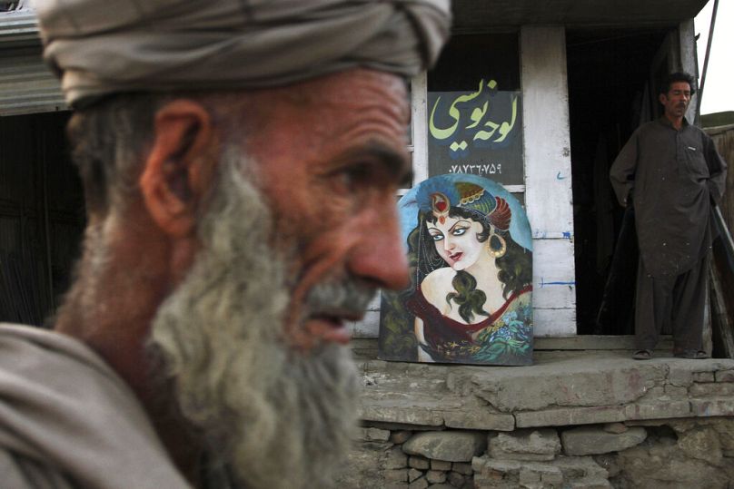 Un vieil homme afghan passe devant un tableau peint représentant une femme devant l'atelier de peinture de Shaker à Kaboul, juin 2011.