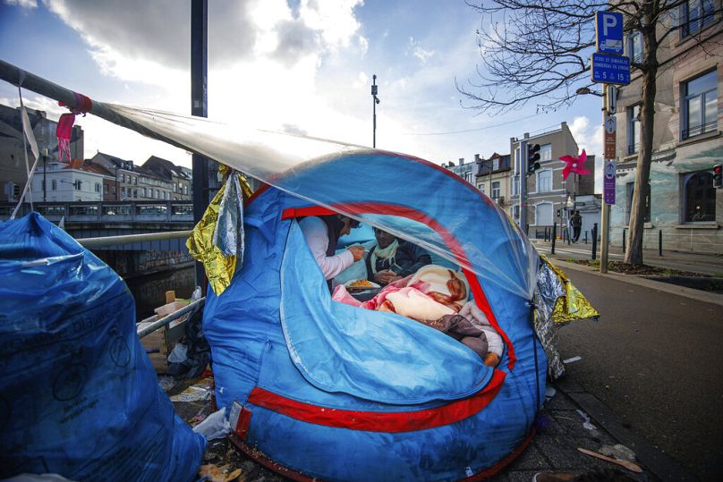 Deux hommes partagent un repas dans un camp de tentes de fortune à l'extérieur du centre d'accueil du Petit Château à Bruxelles, janvier 2023.