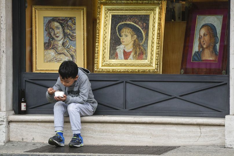 Un enfant apprécie sa glace assis près d'une vitrine vendant des articles religieux à Rome, janvier 2023