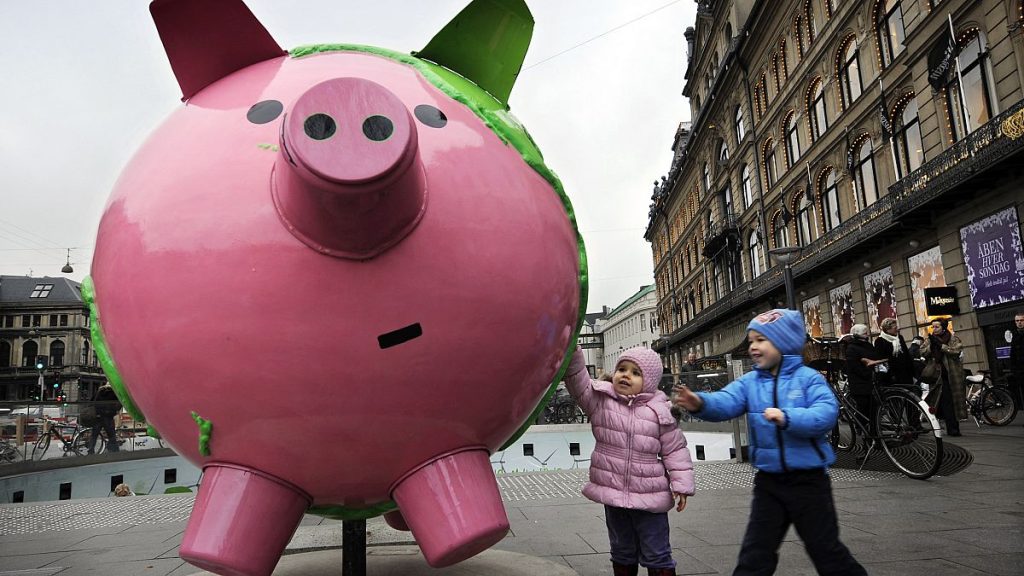 Children touch a giant model globe in the shape of a piggy bank, part of an art installation entitled