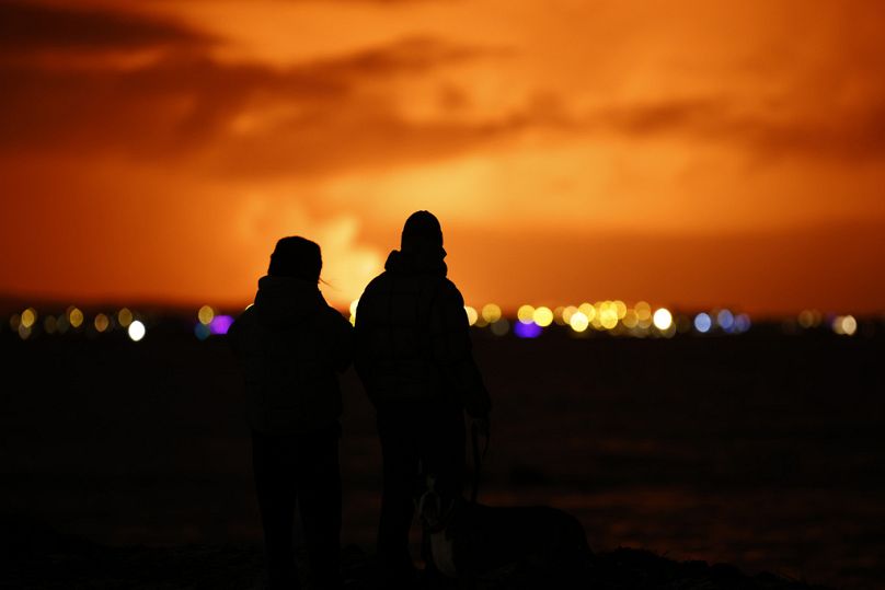 Les gens regardent le ciel nocturne s'illuminer à cause de l'éruption d'un volcan sur la péninsule de Reykjanes, au sud-ouest de l'Islande, vu depuis la capitale Reykjavik.