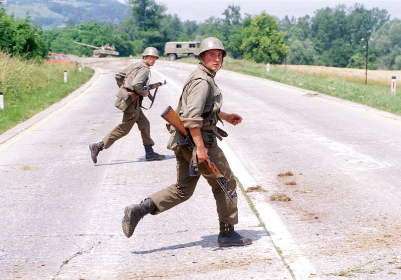 Deux soldats yougoslaves se mettent à l'abri lors d'échanges de tirs avec des membres des forces de défense slovènes près de Brezice, à 24 km de Zagreb, juillet 1991.