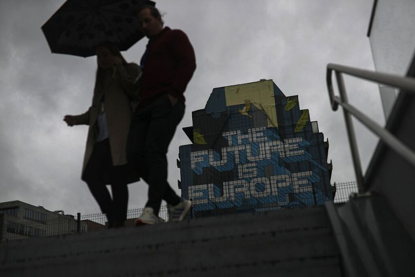 Des gens s'abritent de la pluie en passant devant des œuvres d'art de rue près du siège de la Commission européenne à Bruxelles, en septembre 2019.