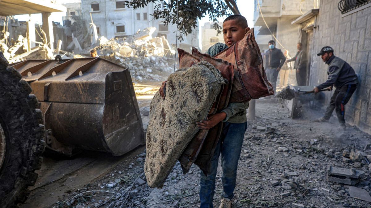 A Palestinian boy carries pillows as a tractor clears debris of buildings destroyed in Israeli bombardments on Rafah, in the southern Gaza Strip