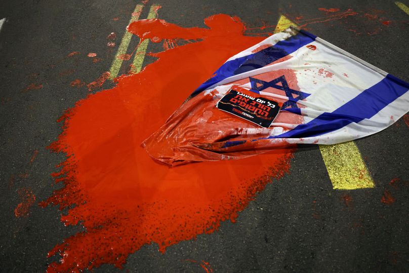 Un drapeau israélien est recouvert de peinture rouge alors que les proches et les partisans des otages détenus par des militants palestiniens manifestent devant le ministère israélien de la Défense à Tel Aviv