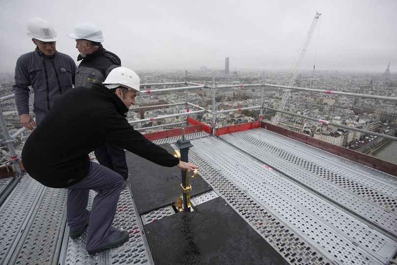 Le président français Emmanuel Macron (à gauche) touche le sommet de la flèche et de la croix nouvellement reconstruites, lors de sa visite aux travaux de reconstruction de la cathédrale Notre-Dame de Paris