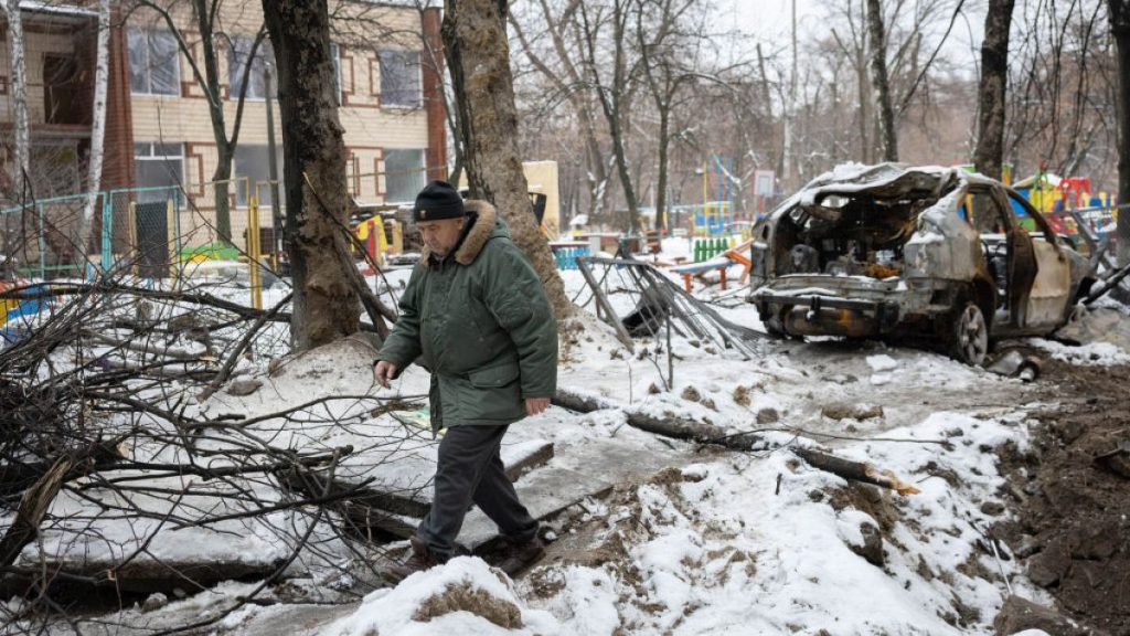 A local resident walks near a crater and a car destroyed by an explosion of an Russian ballistic missile in Kyiv.