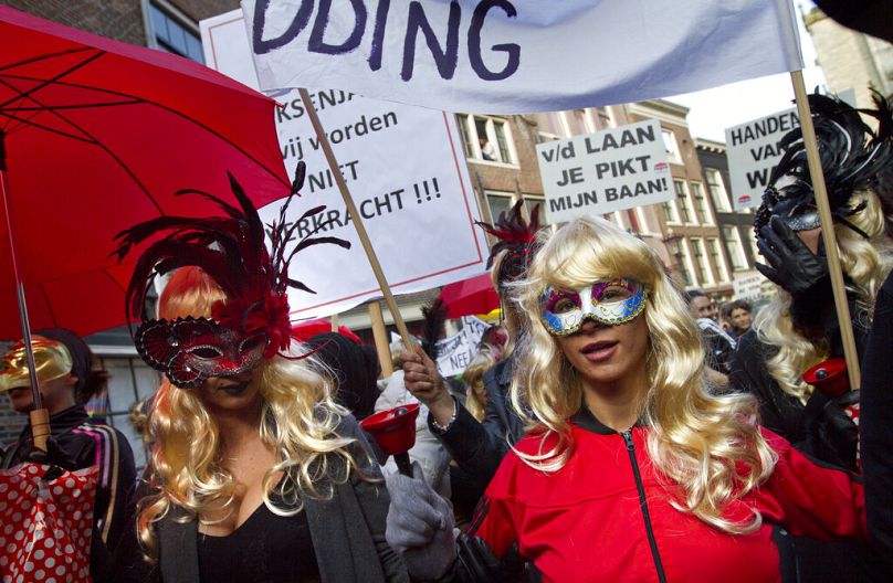 Des femmes masquées brandissent des banderoles alors que les prostituées et leurs sympathisants descendent dans les rues pour protester contre le projet de nettoyage du célèbre quartier rouge de la ville.