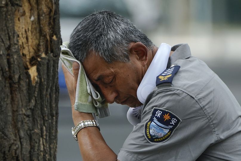 Un agent de sécurité portant un ventilateur électrique autour du cou essuie sa sueur lors d'une chaude journée à Pékin, le lundi 3 juillet 2023.