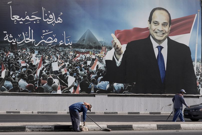 Des ouvriers nettoient la rue sous un panneau publicitaire soutenant le président égyptien Abdel Fattah el-Sissi pour les élections présidentielles, au Caire.