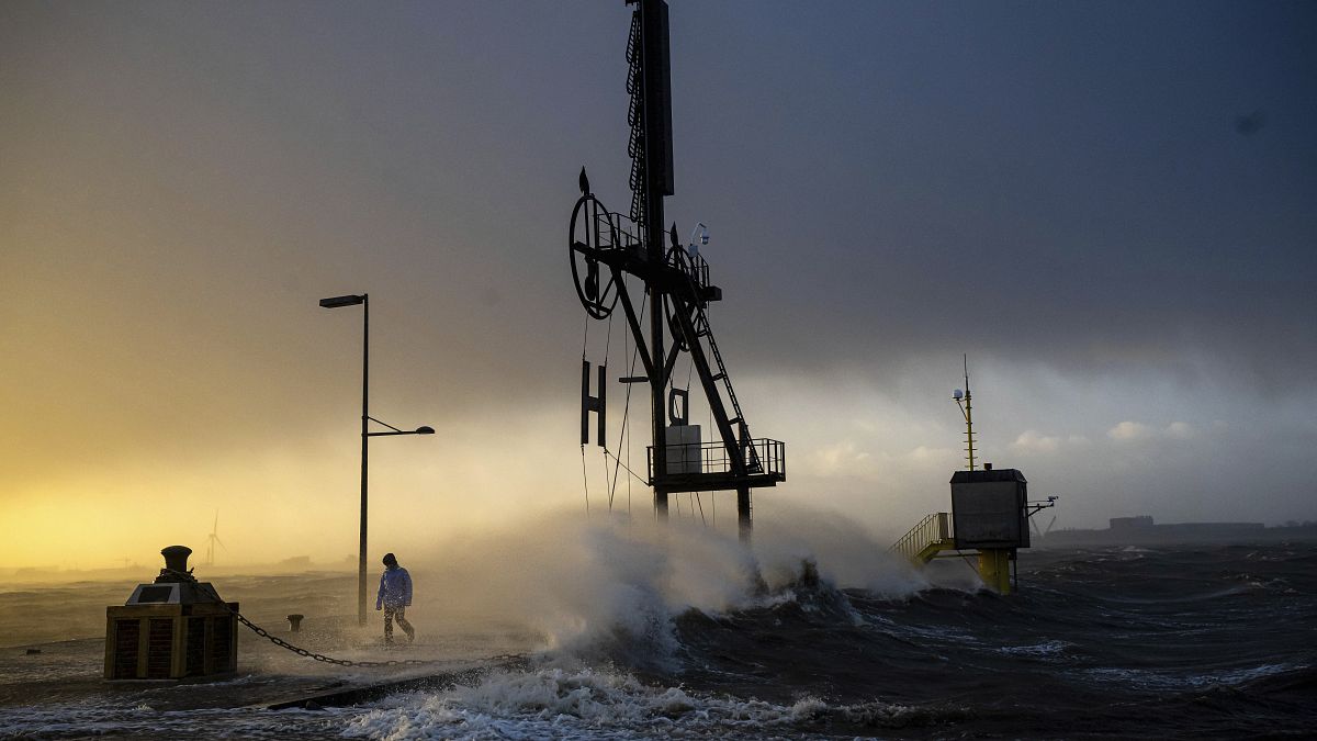 A person walks along the banks of the Weser estuary during a storm surge and waves in Bremerhaven, Germany, Friday 22 Dec 2023