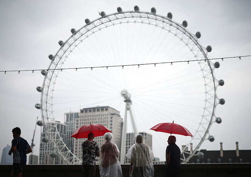 Des piétons s'abritent de la pluie sous des parapluies tout en regardant le monument londonien, le London Eye, depuis Embankment by the River Thames, dans le centre de Londres, le 18 août.