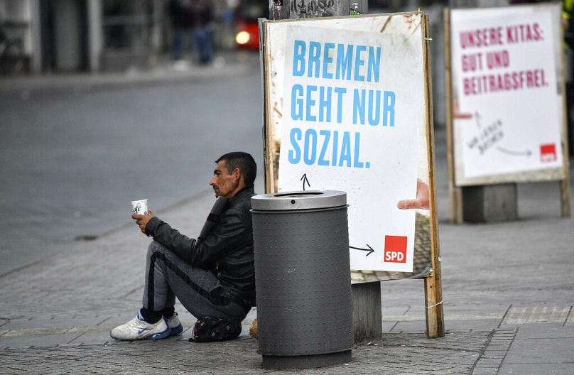 Un homme mendie devant une affiche du SPD indiquant « Brême ne travaille que socialement » pour les élections régionales dans le centre de Brême, en Allemagne, le mardi 14 mai 2019.