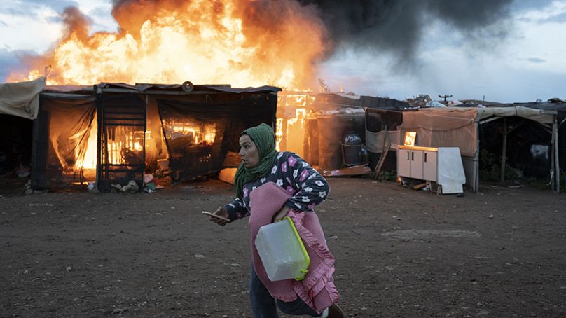 Une femme passe devant des cabanes en feu lors d'un incendie avant d'être expulsée par des policiers à Almeria, en Espagne, le lundi 30 janvier 2023.