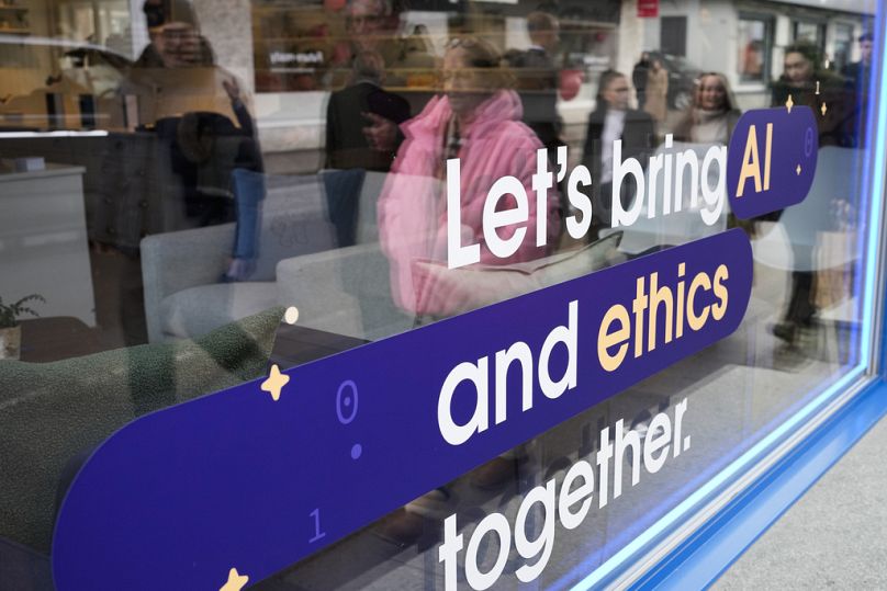 Personnes reflétées dans la fenêtre d'un immeuble de la Promenade de Davos avec un slogan sur l'IA en marge du Forum économique mondial de Davos, janvier 2024.