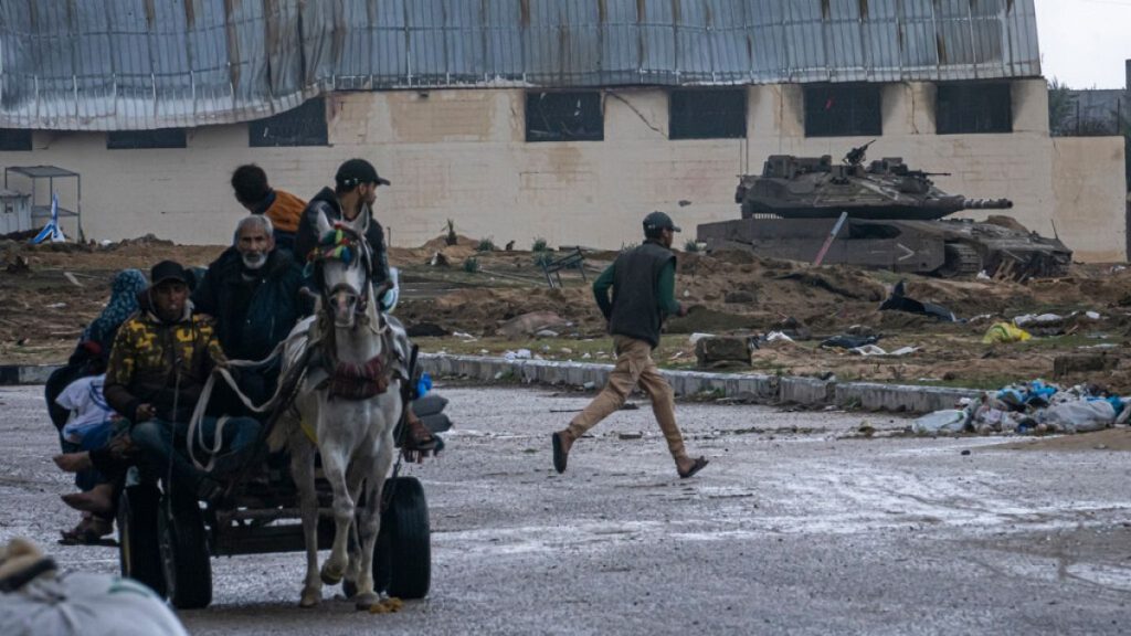 An Israeli army tank takes up position as Palestinians arrive in the southern Gaza town of Rafah after fleeing an Israeli ground and air offensive.