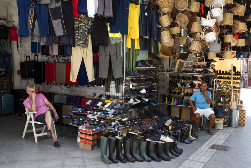 Deux vendeurs sont assis devant des magasins dans une rue commerçante, à Athènes