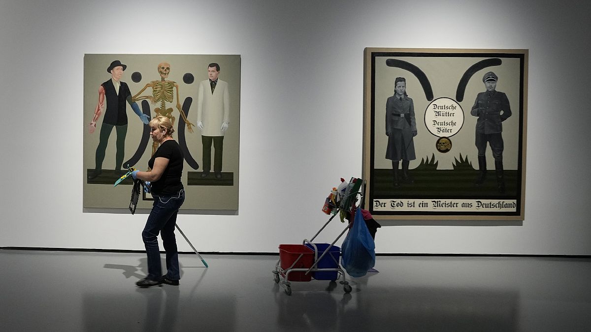 Two works by Polish artist Ignacy Czwartos on display at a 2021 exhibition. The painting on the right reads “German Mothers, German Fathers, Death Is A Master From Germany