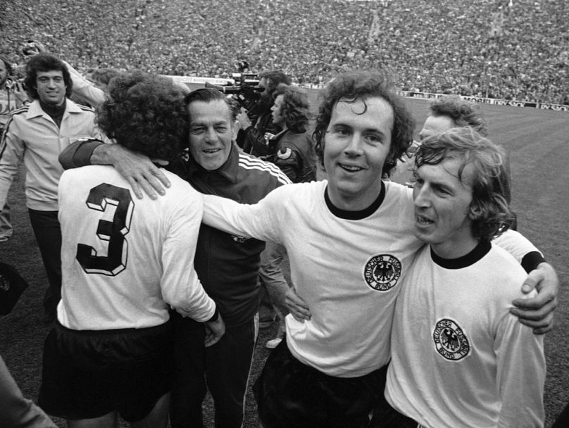 Le capitaine de l'équipe nationale de football d'Allemagne de l'Ouest, Franz Beckenbauer, deuxième à partir de la droite, embrasse son coéquipier, l'attaquant Juergen Grabowski, alors qu'il se promène dans le stade olympique.