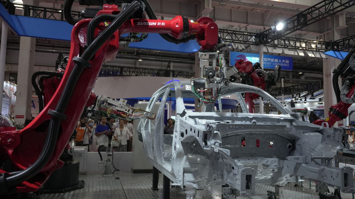 FILE - Visitors look at the robotic arms assembly a vehicle frame during the annual World Robot Conference at the Etrong International Exhibition and Convention Center in the