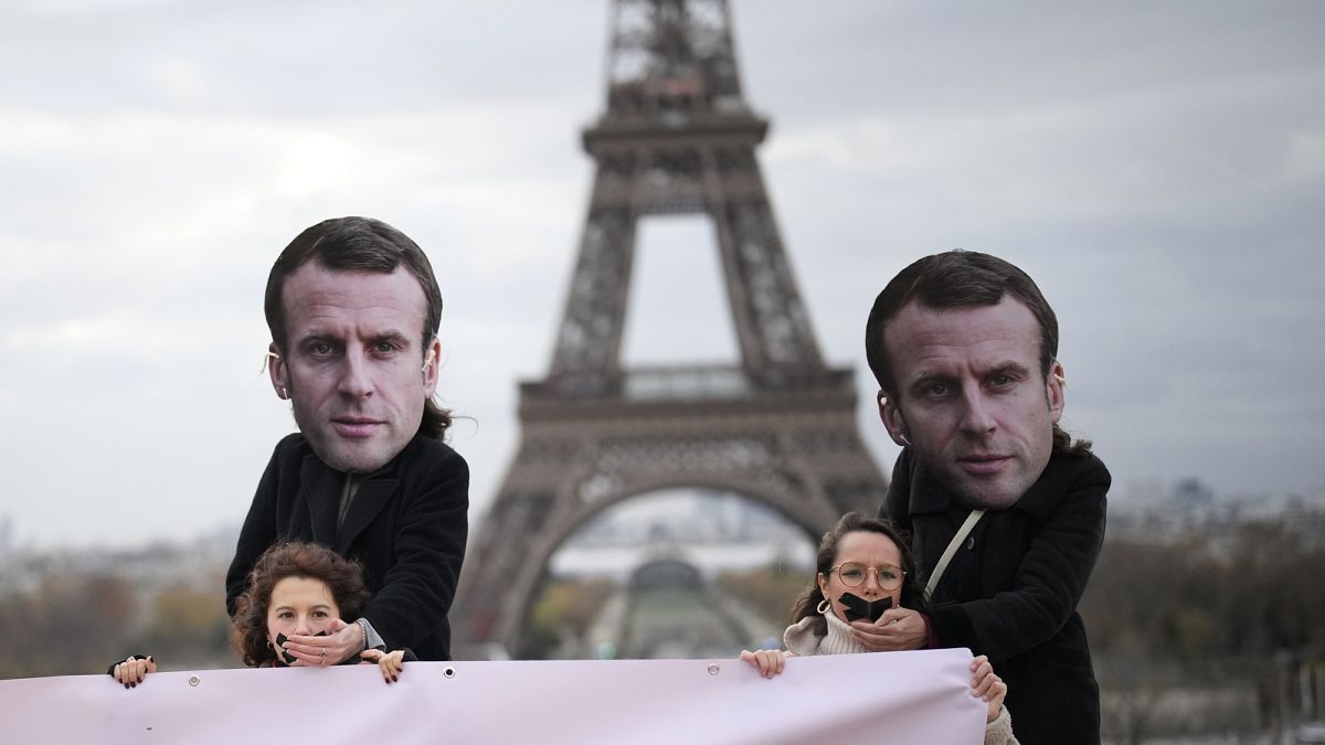Activists wearing masks of Emmanuel Macron place their hands over gagged women during a demonstration in Paris, 24 November 2023