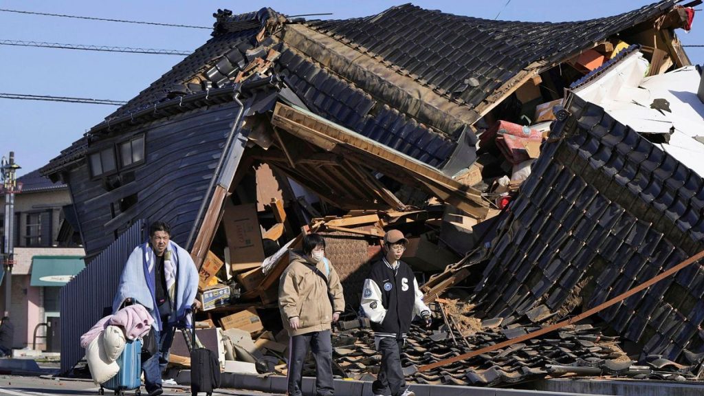 A man carries his belongings past a collapsed house following an earthquake in Wajima, Ishikawa prefecture, Japan, Tuesday, 2 January 2024.