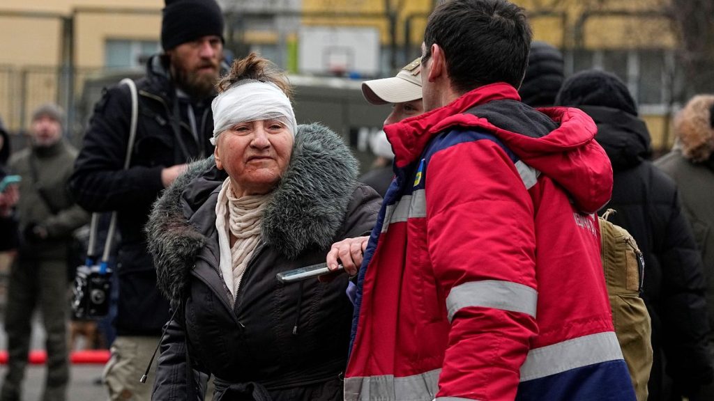 A medical worker helps a woman in a yard of an apartment building destroyed after Russian attack in Kyiv, Ukraine, Wednesday, Feb. 7, 2024.