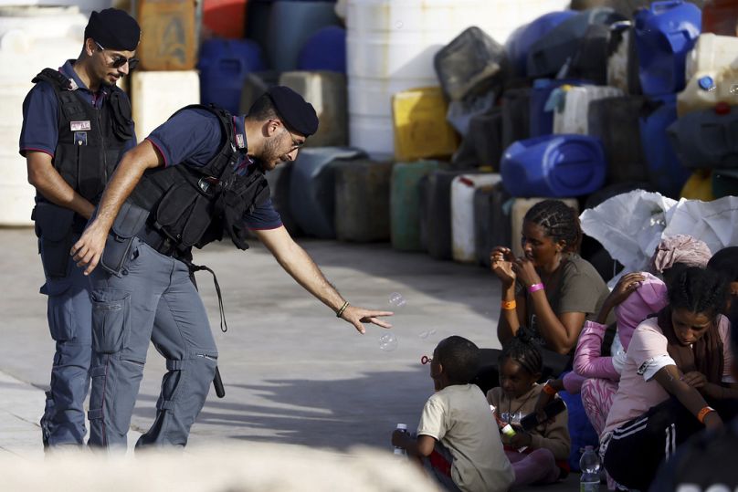 Un policier joue avec un enfant migrant soufflant des bulles de savon dans le port de l'île sicilienne de Lampedusa, novembre 2023