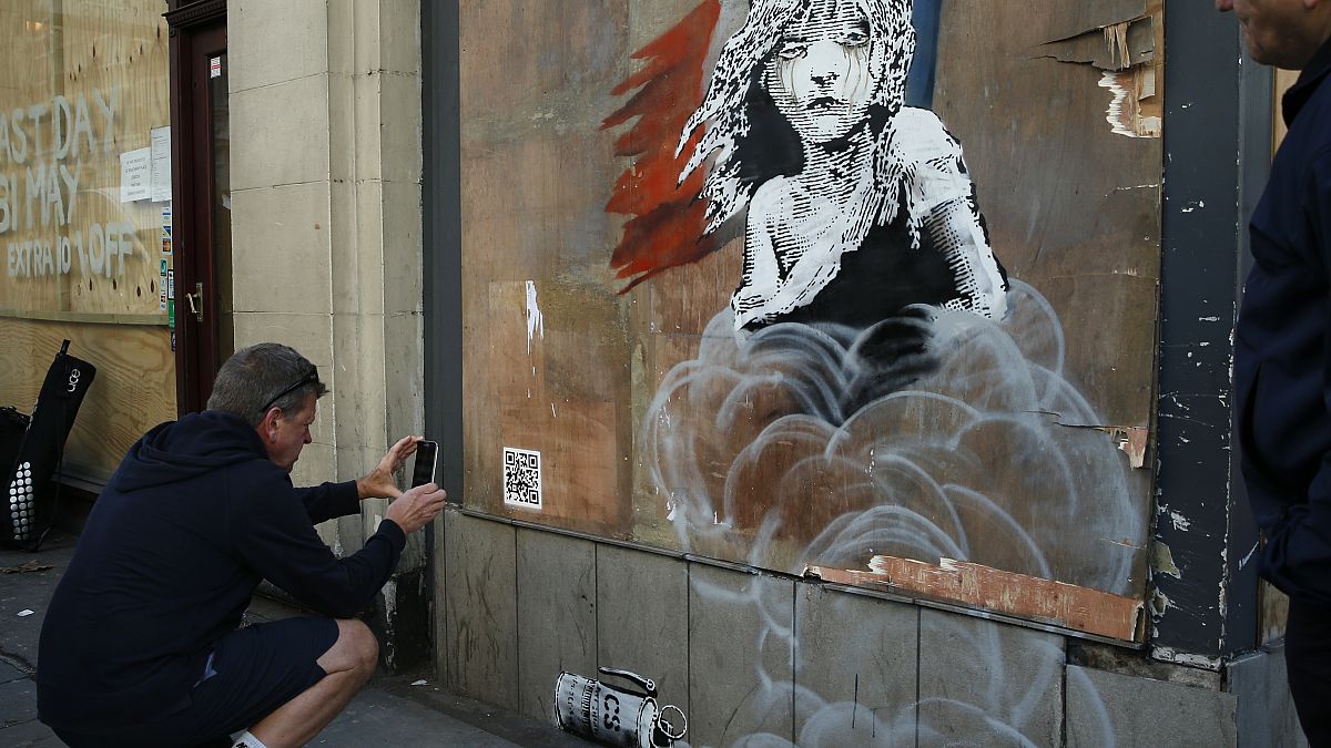 A jogger stops to take photos on his phone of a new artwork by British artist Banksy opposite the French Embassy, in London, 2016.