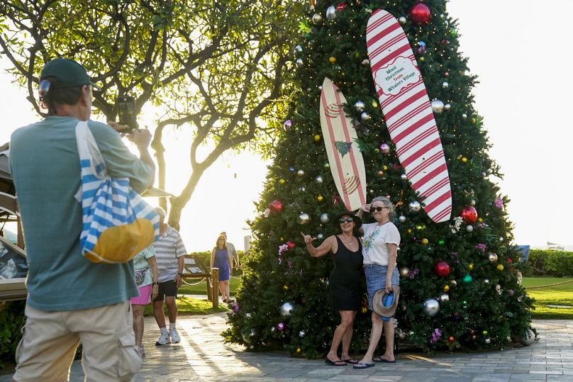 Des gens posent pour une photo devant un sapin de Noël à la plage de Kaanapali, à Hawaï, en décembre, après que les touristes ont commencé à revenir à destination après les incendies meurtriers de Lahaina.