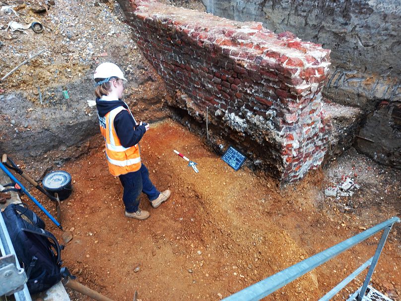 Un archéologue enregistre un grand mur post-médiéval qui a été fouillé.