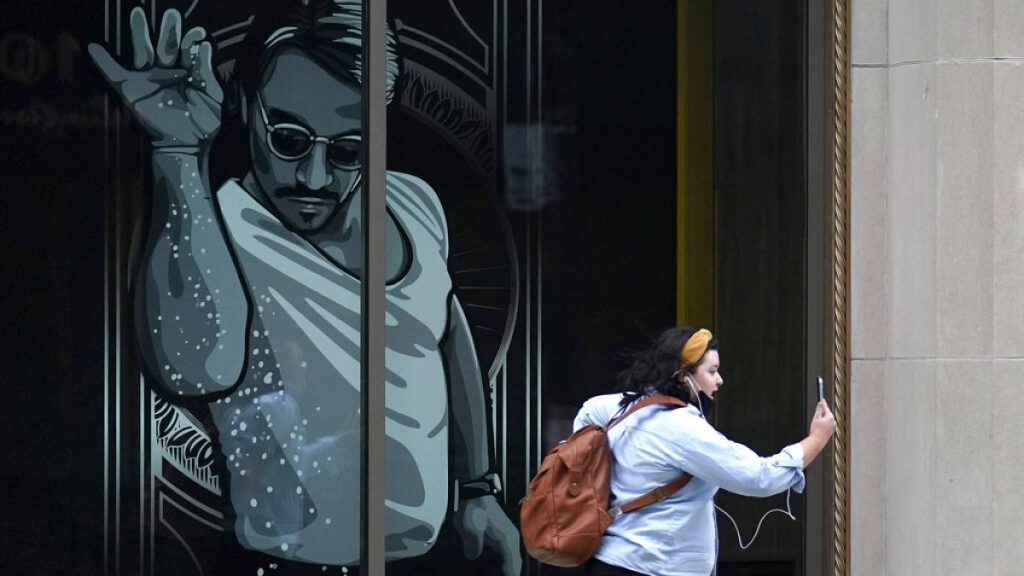 A passer-by uses a mobile device near a window featuring a likeness of chef and social media star Salt Bae outside the Nusr-Et Boston restaurant, Sept. 29, 2020.