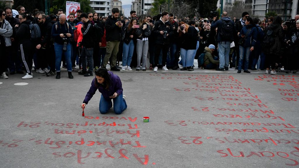 A young woman paints the name of victims from a rail disaster one year ago, in front of parliament, in Athens, Greece, Wednesday, Feb. 28, 2024.