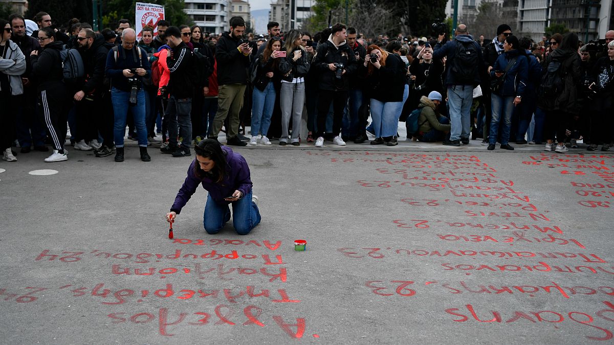 A young woman paints the name of victims from a rail disaster one year ago, in front of parliament, in Athens, Greece, Wednesday, Feb. 28, 2024.