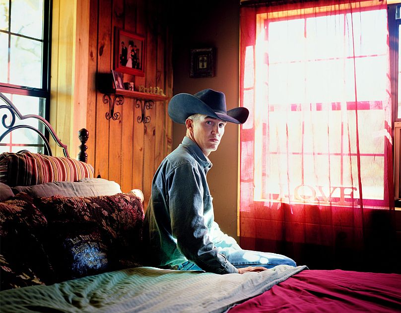 Portrait de Pate Meinzer, un jeune cow-boy fougueux du Texas, assis sur son lit conjugal.