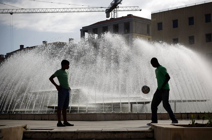 Deux jeunes hommes, vus en silhouette, jouent avec un ballon de football sur la place Martim Moniz de Lisbonne, mars 2011.