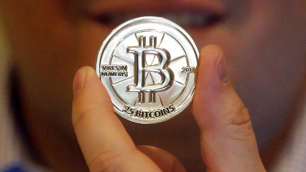 In this April 3, 2013, photo, a man holds a token beaing the symbol of a cryptocurrency at his shop in Sandy, Utah.