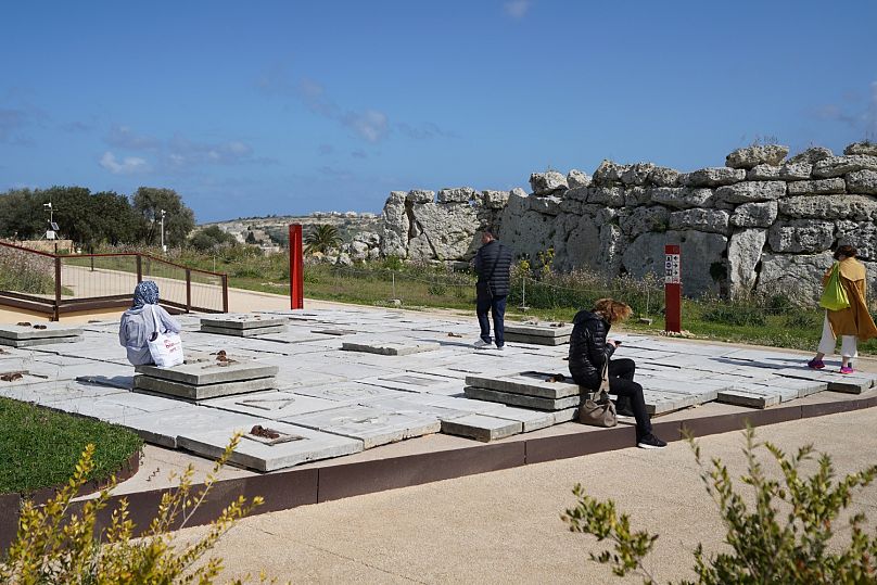 Visiteurs assis et debout sur l'installation « Jardin des cicatrices » d'Ibrahim Mahama, avec le parc archéologique de Ġgantija en arrière-plan.