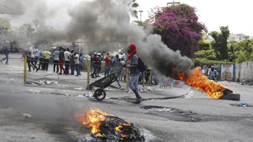 A man pushes a wheelbarrow past burning tires during a protest demanding the resignation of Prime Minister Ariel Henry, in Port-au-Prince, Haiti, Thursday, March 7, 2024.