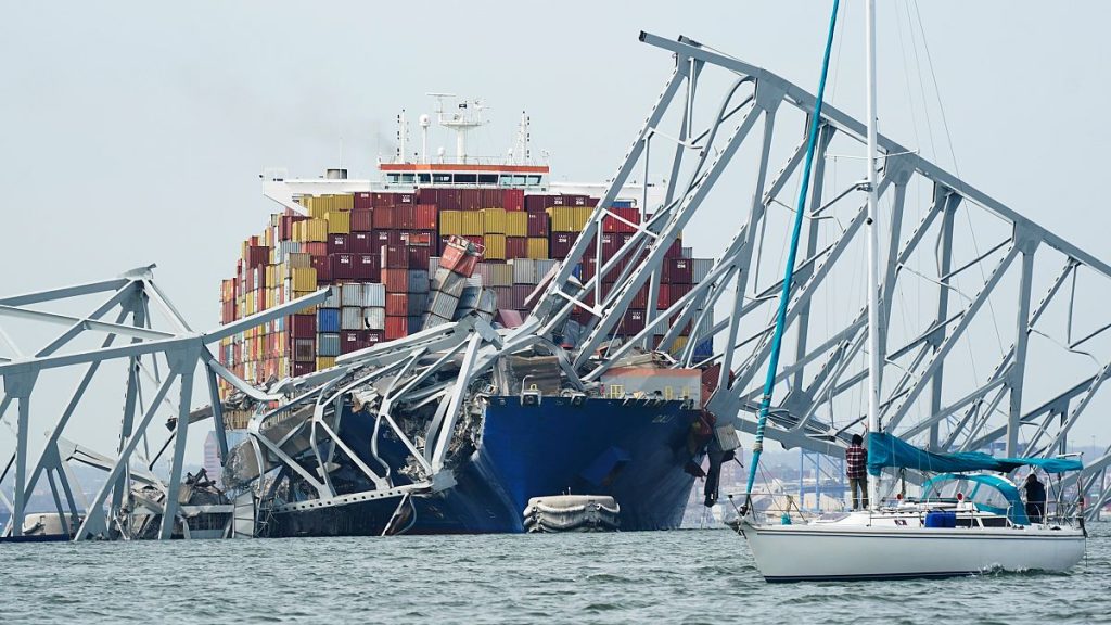 A sailboat passes by a cargo ship is stuck under the part of the structure of the Francis Scott Key Bridge after the ship hit the bridge Tuesday March 26, 2024, in Baltimore.