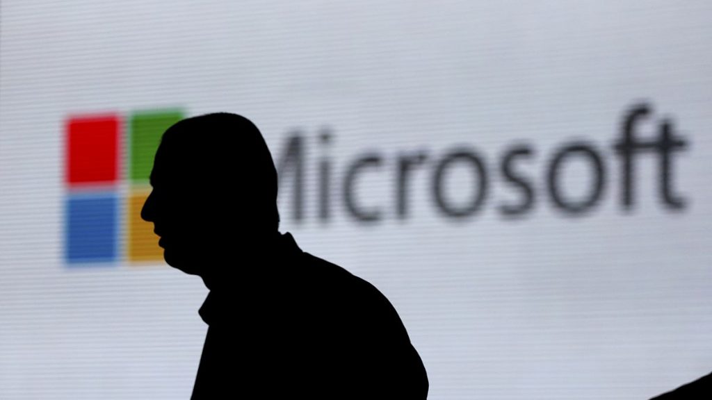 In this Nov. 7, 2017, file photo, an unidentified man is silhouetted as he walks in front of Microsoft logo at an event in New Delhi, India.