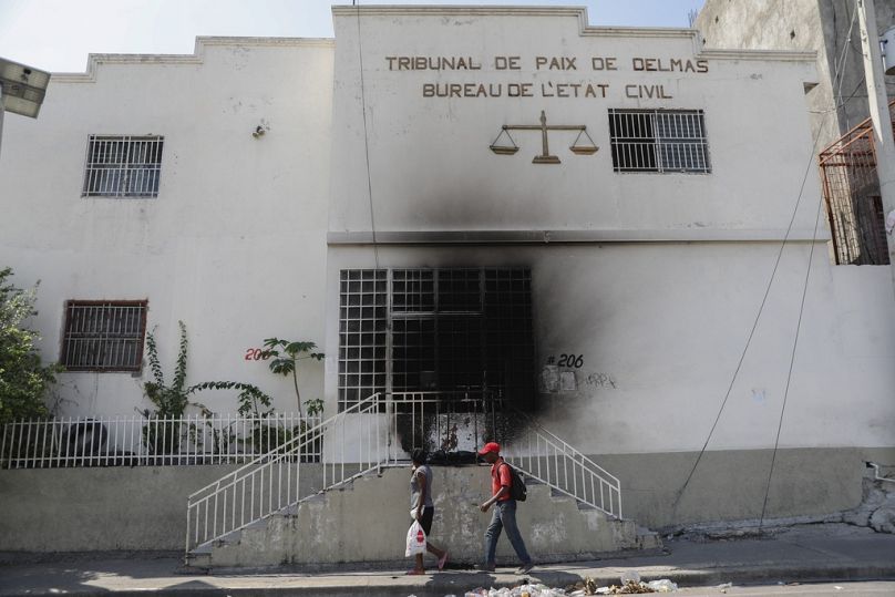 Des piétons passent devant un palais de justice incendié par des gangs quelques instants auparavant dans le quartier Delmas 28 de Port-au-Prince.