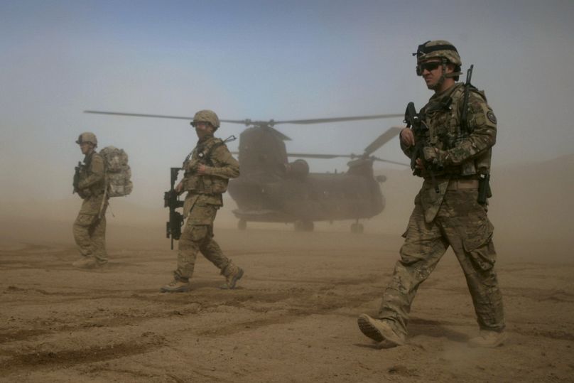 Des soldats de la Force internationale d'assistance à la sécurité (FIAS) dirigée par l'OTAN marchent tandis qu'un hélicoptère Chinook est aperçu à l'arrière-plan à Shindand, Herat, janvier 2012.