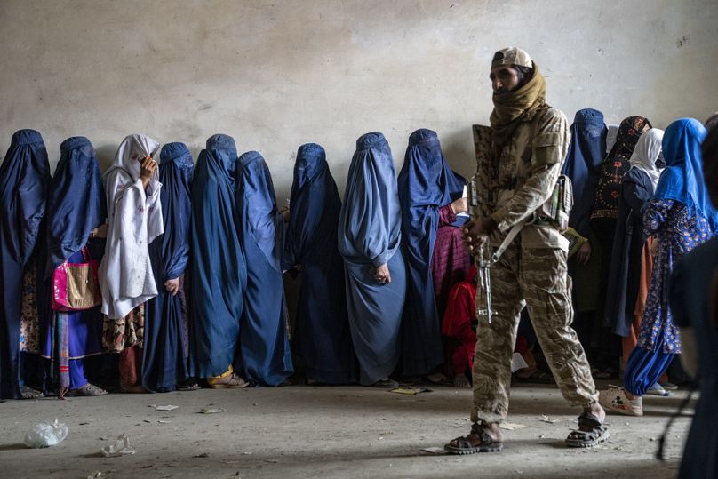 Un combattant taliban monte la garde pendant que des femmes attendent de recevoir des rations alimentaires distribuées par un groupe d'aide humanitaire, à Kaboul, en mai 2023.
